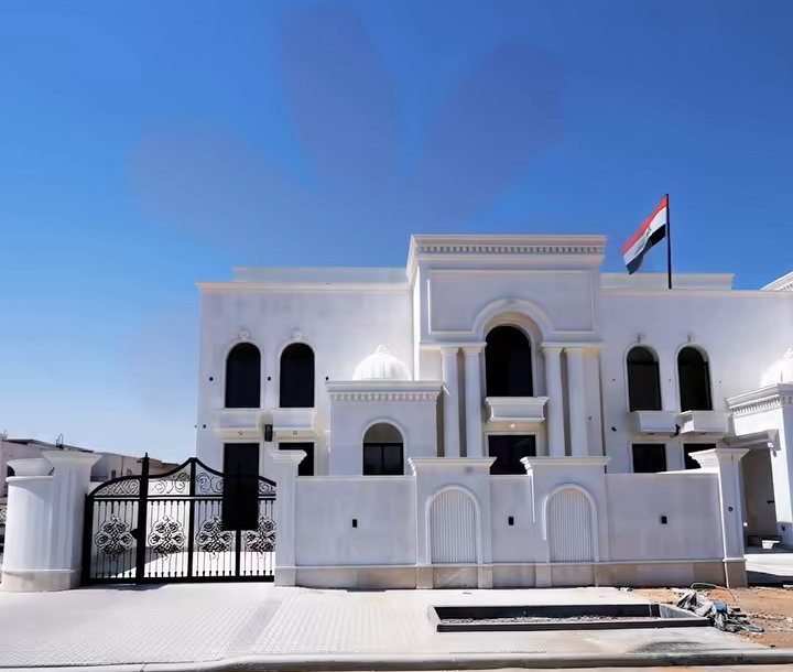 The white school building with arched windows and the Iraqi flag, under a clear blue sky